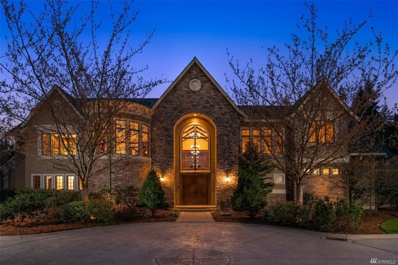 Woodinville home with a stone entry and warmly lit windows at dusk